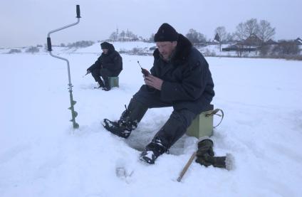 Рыбак сидит возле лунки и ловит рыбу на мармышку.