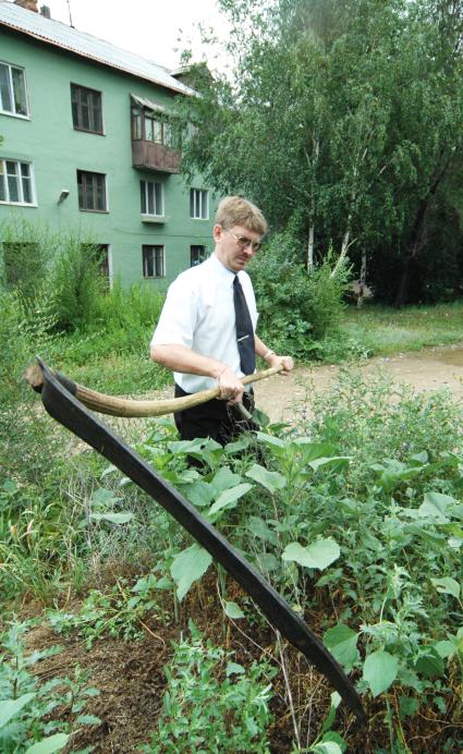 Мужчина в белой рубашке и галстуке косит траву