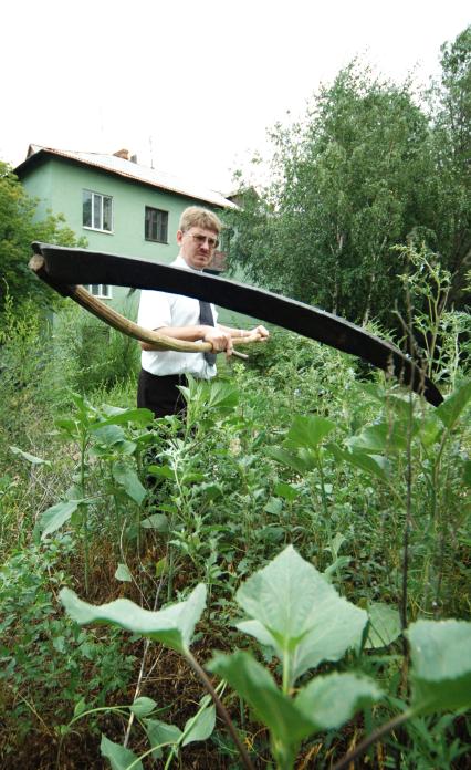 Мужчина в белой рубашке и галстуке косит траву