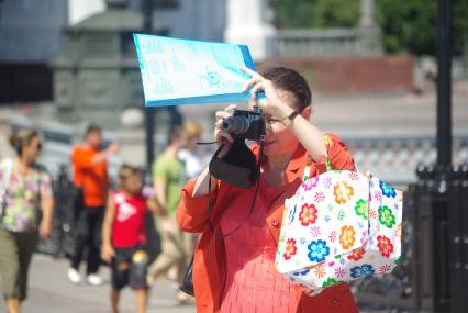 Туристка фотографирует достопримечательности города, документами прикрывая лицо от солнца, 30 июня 2010 года. Жара. Лето. Женщина. Туристка. Фотоаппарат. Солнце. Зной. Достопримечательности. Туризм. Отдых. Папарацци. Документы.