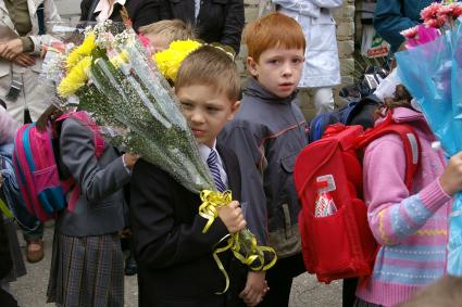 Первоклассник на школьной линейке с цветами груснтно смотрит на уходящее беззаботное детство, 1 сентября 2009 года.Саратов. Школа. Школьники. 1 класс. Форма. Дети. Детство. Ученик. Ученица. Учеба. Цветы. Линейка школьная.