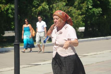 Пожилая женщина с палочкой идёт по городу, на заднем фоне молодая пара мужчина и женщина, 21 июля 2010 года. Старость и молодость, пенсия, пенсионная реформа, зарплата, старушка, бабка, старуха, молодые, будущее, семья, дорога жизни, город, лето, косынка,