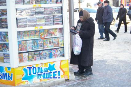 Бабулька в пуховом платке у киоска с дисками выбирает компакт диск со сказками, 26 января 2010 года, Саратов. Бабушка, бабуля, внуки, подарок, сказки,нелицензионные диски, пиратство, пуховый платок, пенсия, старость, пенсионная реформа.