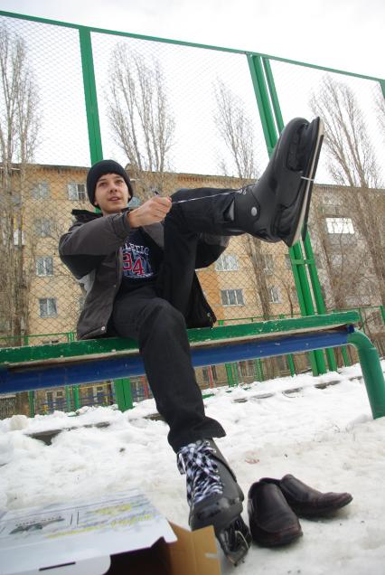 Мальчик одевает коньки сидя на лавочке перед школой, 22 декабря 2010 года, Саратов. школьники, дети, каток, коньки, зима, зимние забавы, каникулы, развлечения, отдых, школа, перемена, урок физкультуры, закалка.