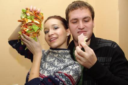 Девушка и парень едят большой бутерброд, Саратов, 23 декабря 2010 года, Саратов. Фаст- фуд, бутерброд, гамбургер, мясо, сыр, хлеб, кетчуп, еда, обед, ланч, завтрак, хозяйка, повар, кулинария, гастрит, ожирение, диета, обжорство, отношения, муж и жена, обед, качество, роспотребнадзор, некачественные продукты, товары