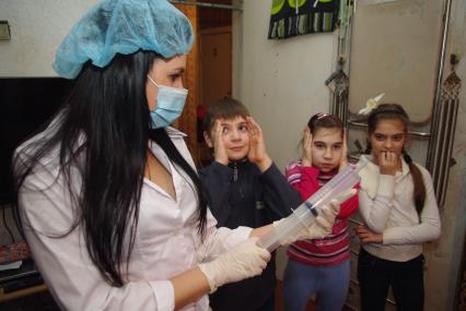 Дети с ужасом смотрят на участкового врача- педиатра с большим шприцом, Саратов, 31 января 2011 года. Дети, карантин, грипп, болезнь, уколы, лечение, участковый врач, педиатр, маска, шприц, больница, школьники.