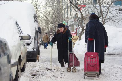 Две женщины с тележками с трудом проходят по нечищенной улице, Москва, 16 февраля 2011 года. Снег, зима, нечищенная дорога, улица, снежный занос.