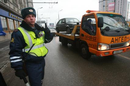 Сотрудник ДПС несет службу на оживленной улице, мимо проезжает автомобиль эвакуатор на борту везущий другой автомобиль ГОЛЬФ. 13 декабря 2007 года.