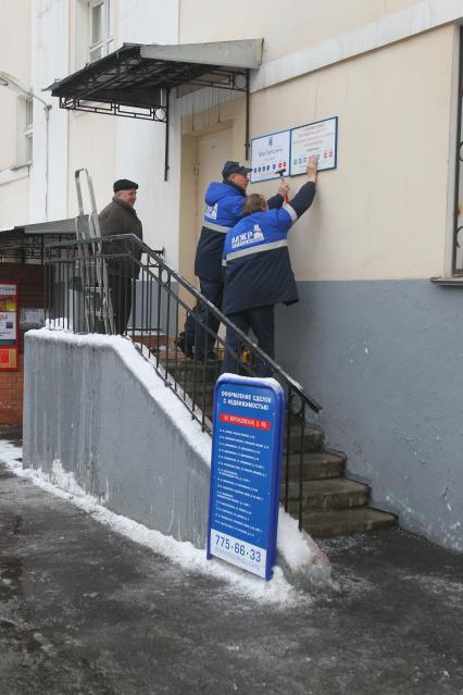 Зима. Двое рабочих прибивают таблички: МОСГОР УСЛУГА. Рядом табличка: ОФОРМЛЕНИЕ СДЕЛОК С НЕДВИЖИМОСТЬЮ. 2 января 2011 года.