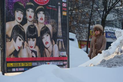 Москвичка проходит мимо рекламного плаката, 16 февраля 2011 года. Снег. Зима. Холод. Мороз. Уборка снега. Сугроб. Коммунальное хозяйство. Гололед. Реклама уличная.