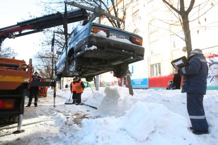 Эвакуатор поднимает автомобили, стоящие вдоль дороги, для очистки под ними снега, Москва, 2 марта 2011 года.