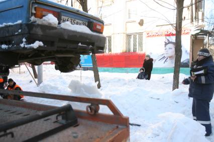 Эвакуатор поднимает автомобили, стоящие вдоль дороги, для очистки под ними снега, Москва, 2 марта 2011 года.