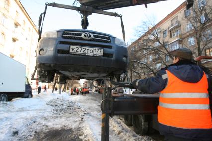 Эвакуатор поднимает автомобили, стоящие вдоль дороги, для очистки под ними снега, Москва, 2 марта 2011 года.