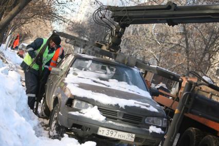 Эвакуатор поднимает автомобили, стоящие вдоль дороги, для очистки под ними снега, Москва, 2 марта 2011 года.