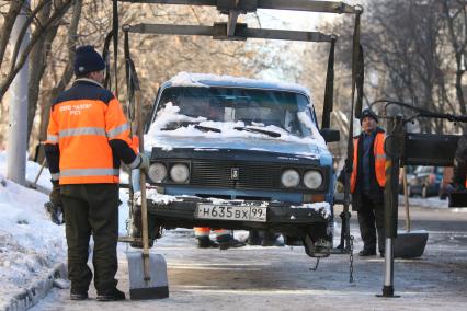 Эвакуатор поднимает автомобили, стоящие вдоль дороги, для очистки под ними снега, Москва, 2 марта 2011 года.