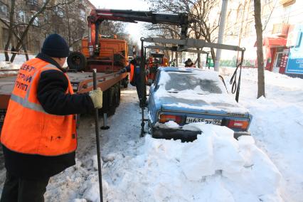 Эвакуатор поднимает автомобили, стоящие вдоль дороги, для очистки под ними снега, Москва, 2 марта 2011 года.