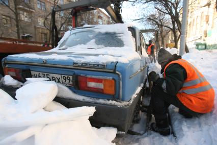 Эвакуатор поднимает автомобили, стоящие вдоль дороги, для очистки под ними снега. 2 марта 2011 года.