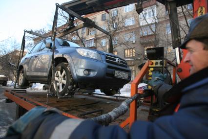 Эвакуатор поднимает автомобили, стоящие вдоль дороги, для очистки под ними снега, Москва, 2 марта 2011 года.