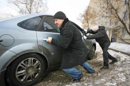 Автомобиль застрял в глубоком снегу. Люди, мужчина и женщина выталкивают машину. 3 марта 2011 года.