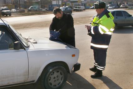 Мужчина из хозяйственно сумки на капоте машины достает документы для гаишника, Саратов, 4 апреля 2008 года.