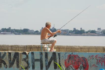 На бетонной плите у реки сидит рыбак с удочкой, Саратов, 31 мая 2010 года