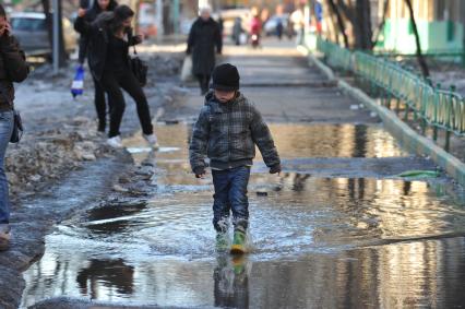 04 апреля 2011 г. Россия, Москва. Мальчик в резиновых сапогах идет по луже.