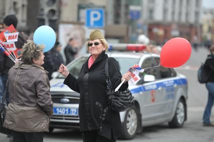 Женщина в военной пилотке с флажками в руках танцует на улице города, Москва, 1 мая 2011 года