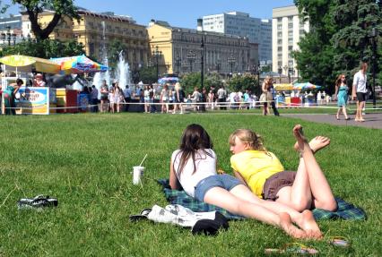 Две девушки отдыхают лежа в центре города на газоне. Мимо проходят люди. 2 июня 2011 года.