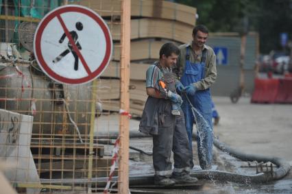 Гастарбайтеры из шланга поливают асфальт на стройке, Москва, 28 июня 2011 года