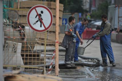 Гастарбайтеры из шланга поливают асфальт на стройке, Москва, 28 июня 2011 года