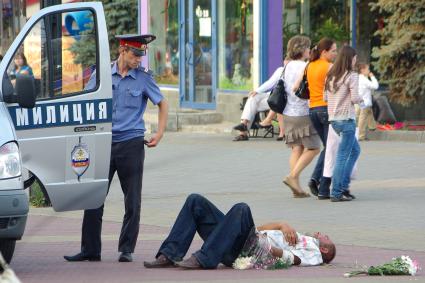 Полицейский стоит у машины, перед ним лежит мужчина с цветами, Челябинск, 15 июля 2011 года.