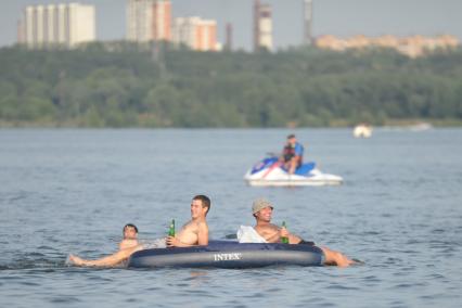 Молодые люди с пивом в руках на надувном матрасе плавают по Москве- реке, Москва, 24 июля 2011 года.