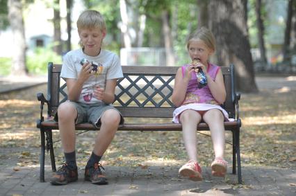 Дети на лавочке в парке едят мороженое, Москва, 27 июля 2011 года.