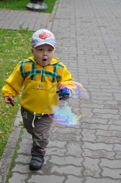 Маленький мальчик, ребенок, бежит по дорожке за мыльным пузырем.