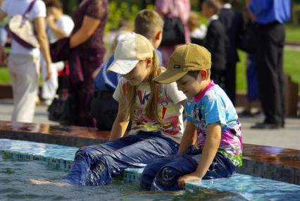 Двое детей, мальчик и девочка сидят в фонтане опустив ноги в воду. 1 сентября 2008 года. Новосибирск.