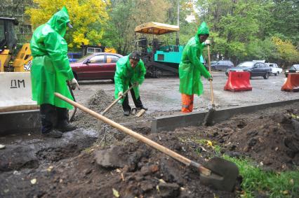 Гастарбайтеры в дождевиках в дождь занимаются установкой бордюрных плит, 23 сентября 2011 года, Москва