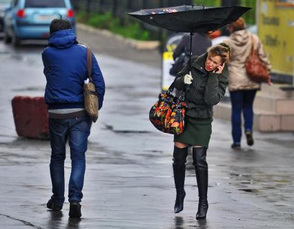 В Москве сильный ветер с дождем. У девушки вырывает зонт ветром, она пытается разговаривать по телефону. 11 октября  2011 года.