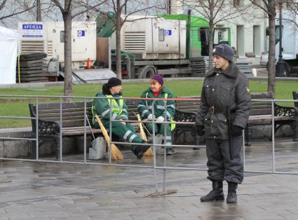 Полицейский стоит рядом с уборщиками. 5 декабря 2011 года.