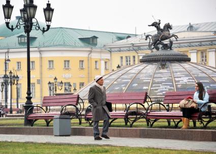 Москва центр города, люди. Мужчина идет по Манежной площади мимо молодой девушки, которая сидит на скамейке. 15 Декабря 2011 года