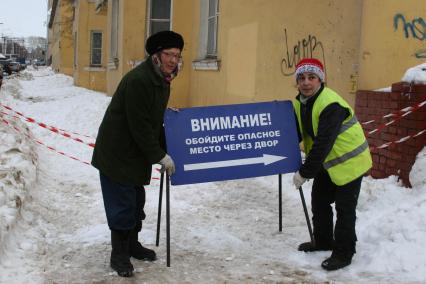 Две женщины перетаскивают указатель с надписью ВНИМАНИЕ! ОБОЙДИТЕ ОПАСНОЕ МЕСТО ЧЕРЕЗ ДВОР. Уфа. 17 марта 2011 года.