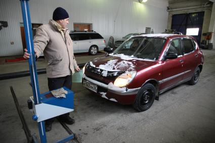 Станция технического осмотра. Легковой автомобиль проходит технический осмотр на станции техосмотра. На снимке: Мужчина проверят свет фар. 20 января 2012 года.