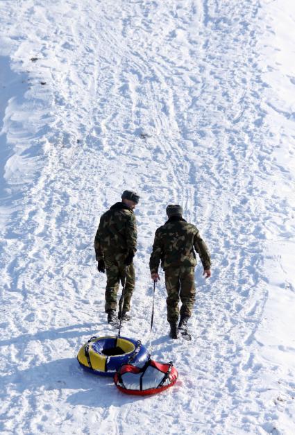 Два солдата везут ватрушки в горку чтобы кататься со снежной горки.