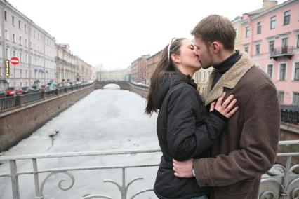 Молодая пара стоит на мосту и целуются.
