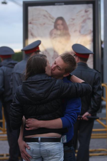 Мужчина и женщина целуются на улице. На заднем плане стоят представители охраны правопорядка (полицейские).