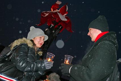 Мужчина и женщина стоят друг напротив друга, в руках держат свечки в одноразовых пластиковых стаканчиках.
