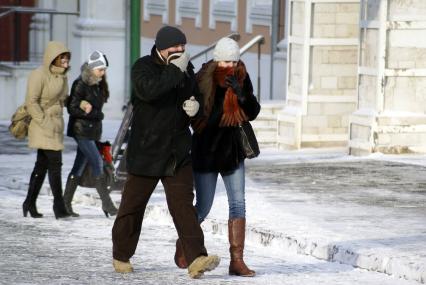 Молодая пара гуляет закрываясь шарфами от мороза.