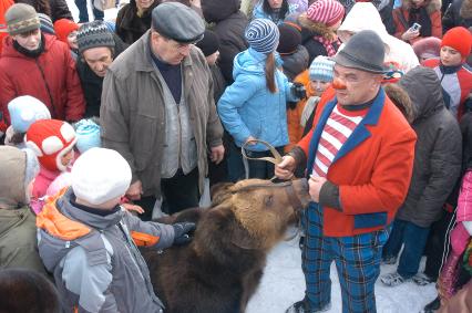 Мужчина стоит посреди зевак с дрессированным медведем.