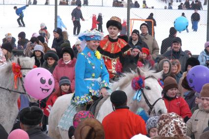 Мужчина и женщина в национальных праздничных одеждах на лошадях посреди толпы людей.