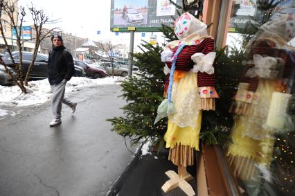 Молодой человек идет по улице города мимо витрины, украшенной чучелом Масленицы, Мосува, 21 февраля 2012