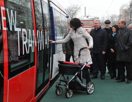 В Москве состоялась презентация трамвая нового поколения, совместная разработка франзузской фирмы `Alstom` и `Трансмашхолдинг`. На снимке: женщина с коляской открывает двери трамвая, на заднем плане мэр Москвы Сергей Собянин и чрезвычайный и полномочный посол Франции в России господин Жан де Глиниасти (четвертый и третий на втором плане соответственно).